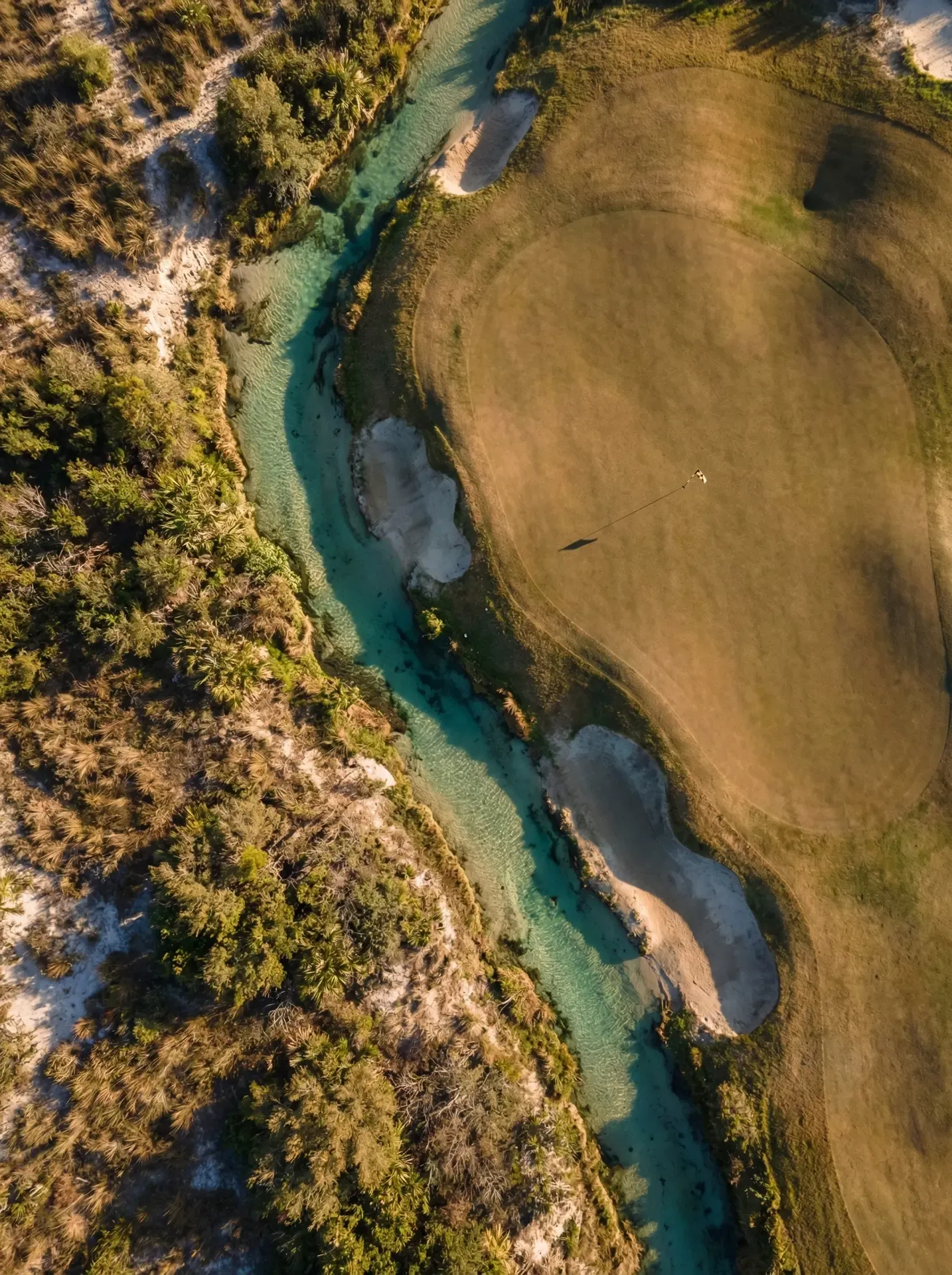 Aerial view of a golf green meeting untouched wilderness, divided by a clear spring-fed creek